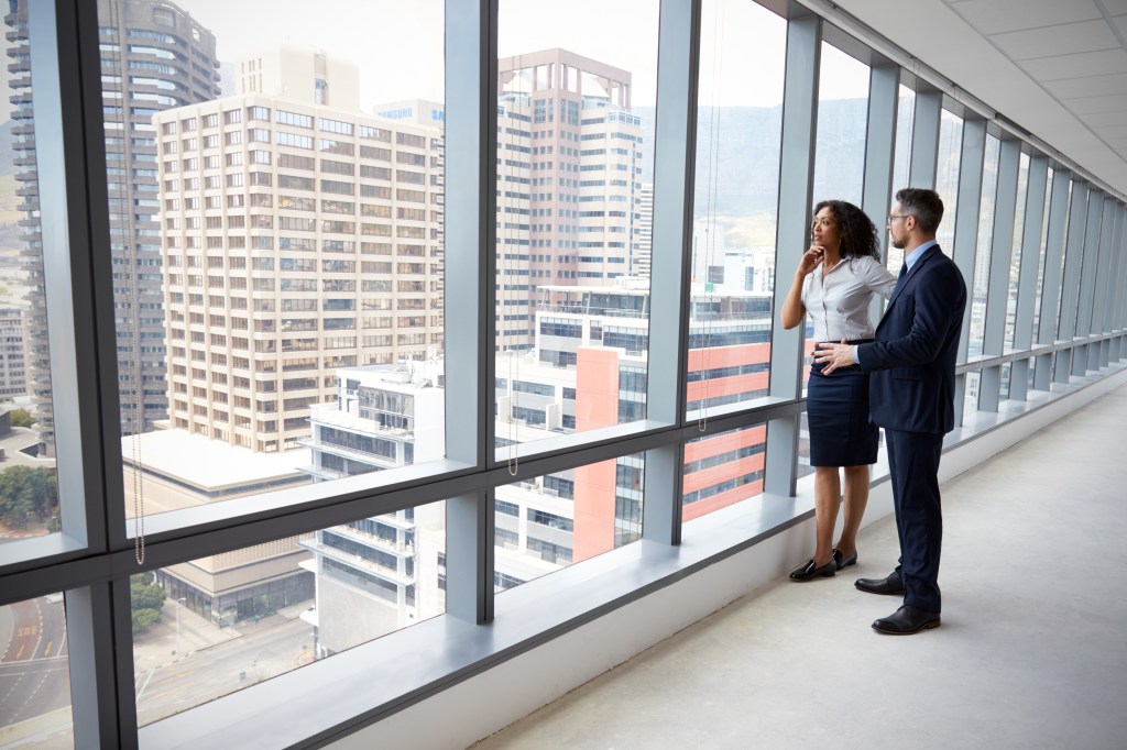 Two professionals looking out over the city skyline from a high-rise office window